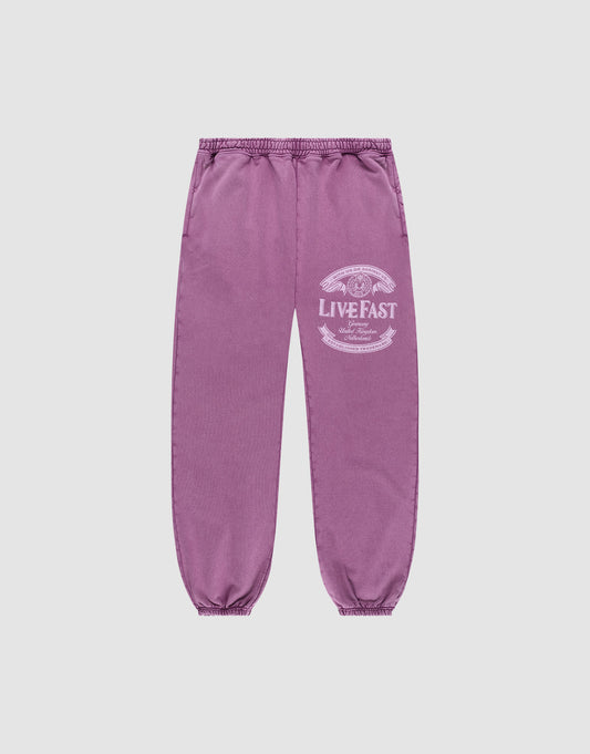 Die Loyal Loose Jogger von LIVE FAST DIE YOUNG sind lila Jogginghosen aus Baumwolle mit elastischem Bund und Bündchen, Vintage-Waschung und weißem LIVE FAST-Print am Oberschenkel, präsentiert vor grauem Hintergrund. | plain