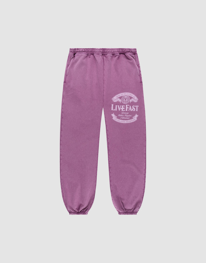 Die Loyal Loose Jogger von LIVE FAST DIE YOUNG sind lila Jogginghosen aus Baumwolle mit elastischem Bund und Bündchen, Vintage-Waschung und weißem LIVE FAST-Print am Oberschenkel, präsentiert vor grauem Hintergrund. | plain