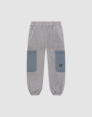 The LIVE FAST DIE YOUNG Live Fast Fleece Pants are light gray wide-fit sweatpants with an elastic waistband and cuffs, two blue nylon thigh pockets—including one with a small black and white logo label—set against a plain white background. | plain