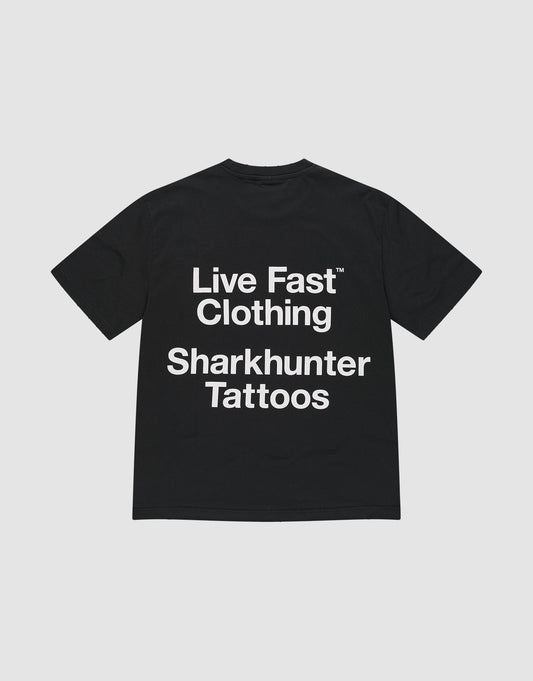 The LFDY Sharkhunter Tee by LIVE FAST DIE YOUNG is a black, soft Baumwolle T-shirt with bold white “Sharkhunter Tattoos” text on the back, oversize fit, and subtle distressing. Shown laid flat on a plain light background.