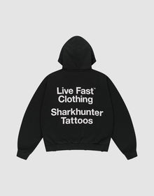 The LFDY Sharkhunter Hooded by LIVE FAST DIE YOUNG is a black oversized cotton hoodie with the hood up, shown flat on a light background. A large white back print reads: Live Fast Clothing Sharkhunter Tattoos. | plain