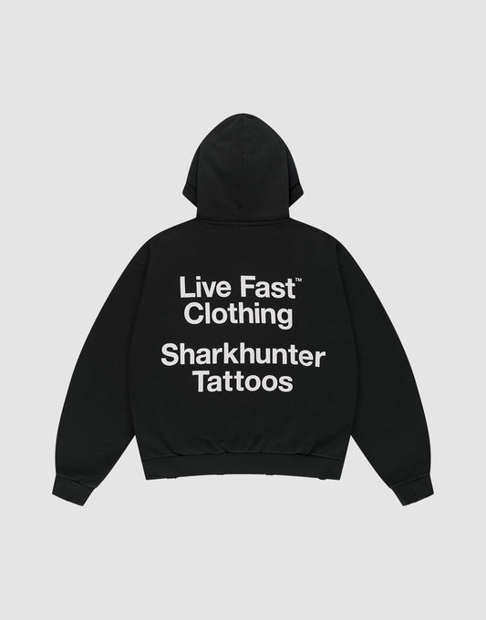 The LFDY Sharkhunter Hooded by LIVE FAST DIE YOUNG is a black oversized cotton hoodie with the hood up, shown flat on a light background. A large white back print reads: Live Fast Clothing Sharkhunter Tattoos.