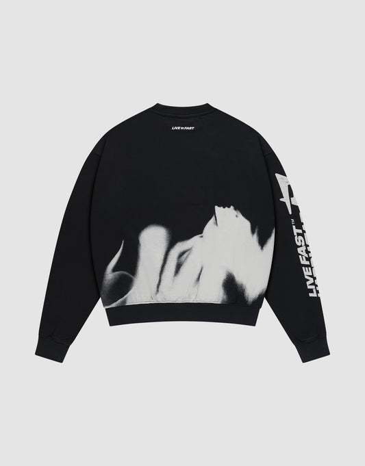 The LFDY Mystic Sweater by LIVE FAST DIE YOUNG is a black, oversized 100% cotton sweatshirt with white flame designs on the lower back and "LIVE FAST" printed on the front and back, shown against a plain light gray background.