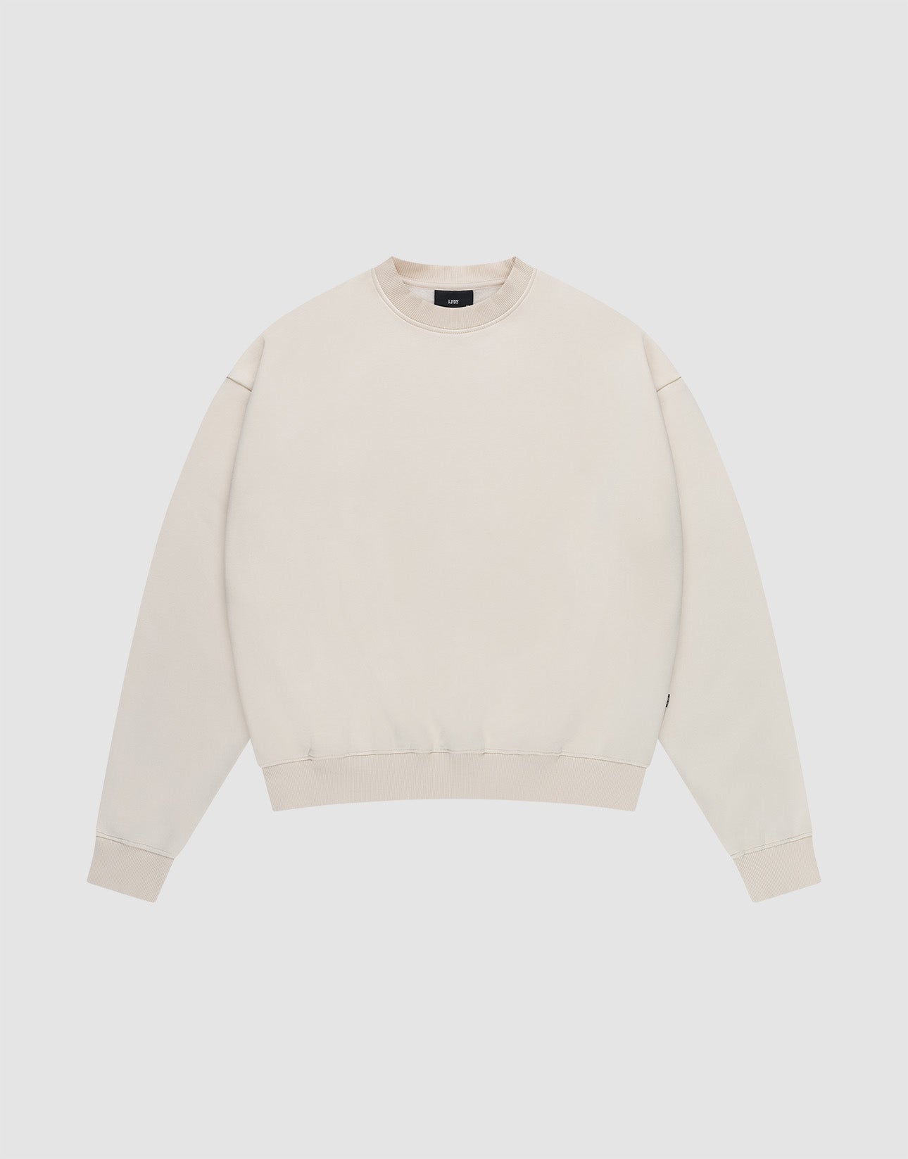 The LIVE FAST DIE YOUNG Basic Blank Sweater is a light beige, oversized crewneck with long sleeves, ribbed cuffs, hem, and collar, made from a soft cotton-polyester blend with a subtle flag label. Shown laid flat on a white background.