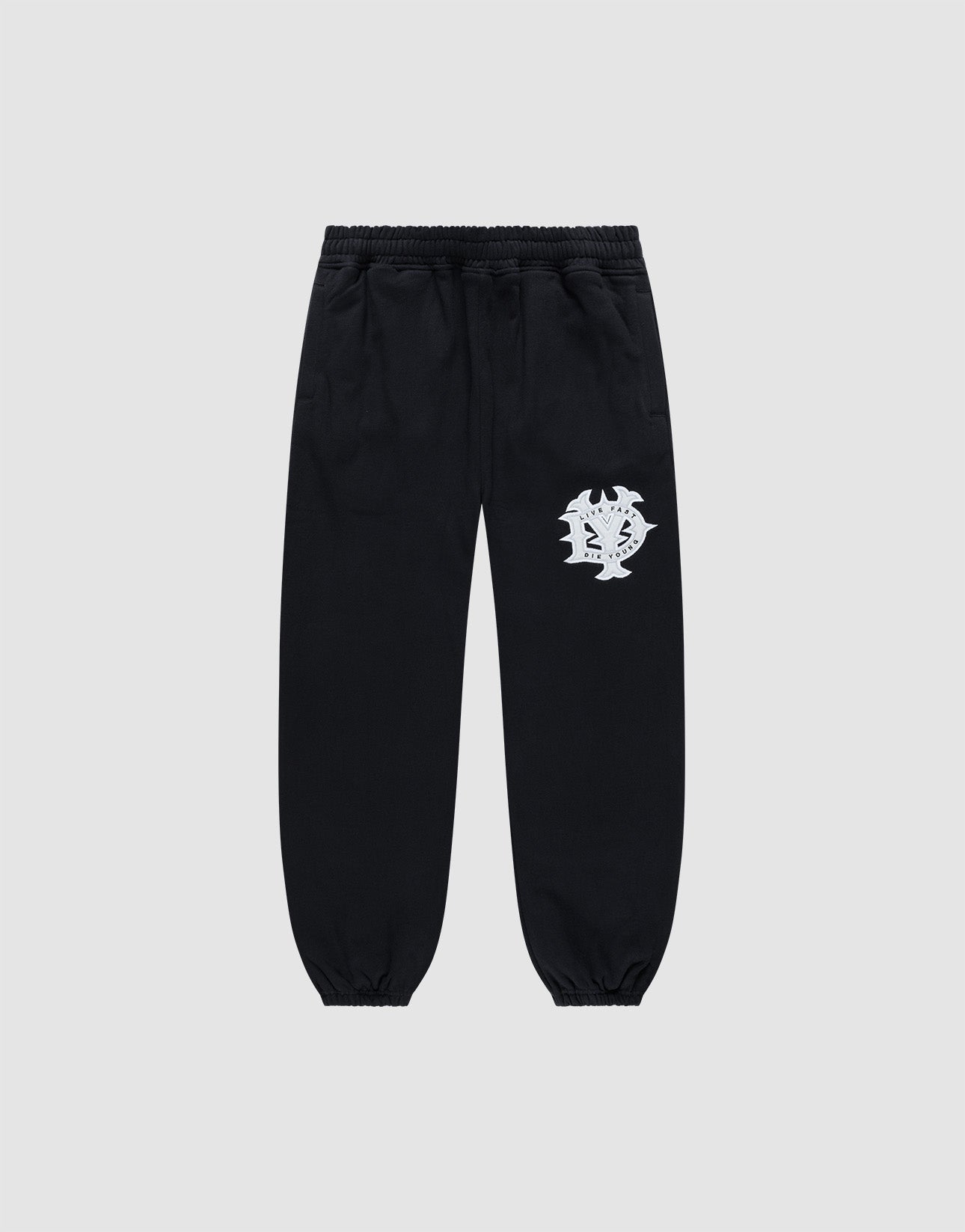 The DY Loose Jogger by LIVE FAST DIE YOUNG are black sweatpants with a loose fit, elastic waistband, cuffs, and a white abstract face graphic on the upper left thigh. Made from soft cotton, shown against a plain light gray background.