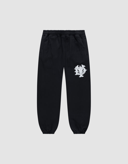 The DY Loose Jogger by LIVE FAST DIE YOUNG are black sweatpants with a loose fit, elastic waistband, cuffs, and a white abstract face graphic on the upper left thigh. Made from soft cotton, shown against a plain light gray background.