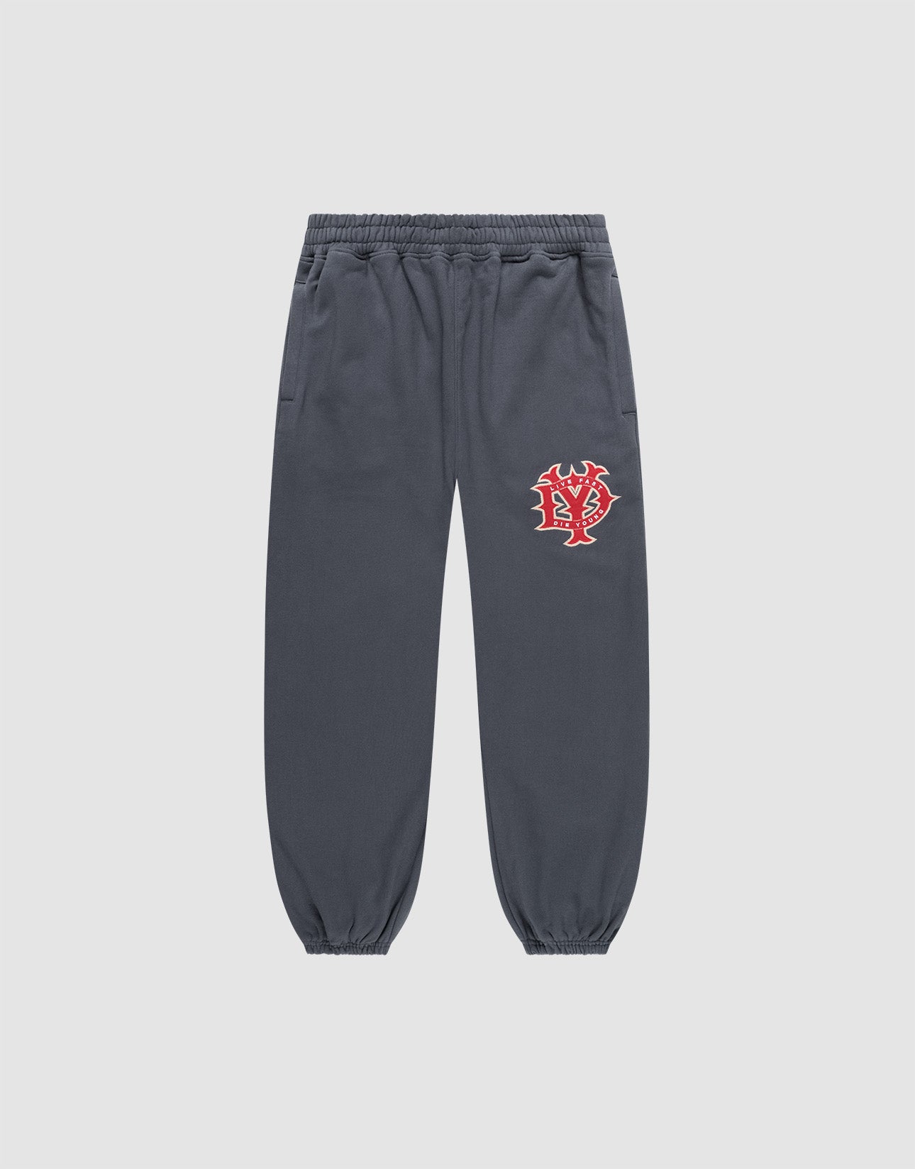 The DY Loose Jogger von LIVE FAST DIE YOUNG in Dunkelgrau ist eine locker geschnittene Sweatpants aus Baumwolle mit Elastikbund, Bündchen, Seitentaschen und rot-weißem Grafikprint am linken Oberschenkel vor hellem Hintergrund.