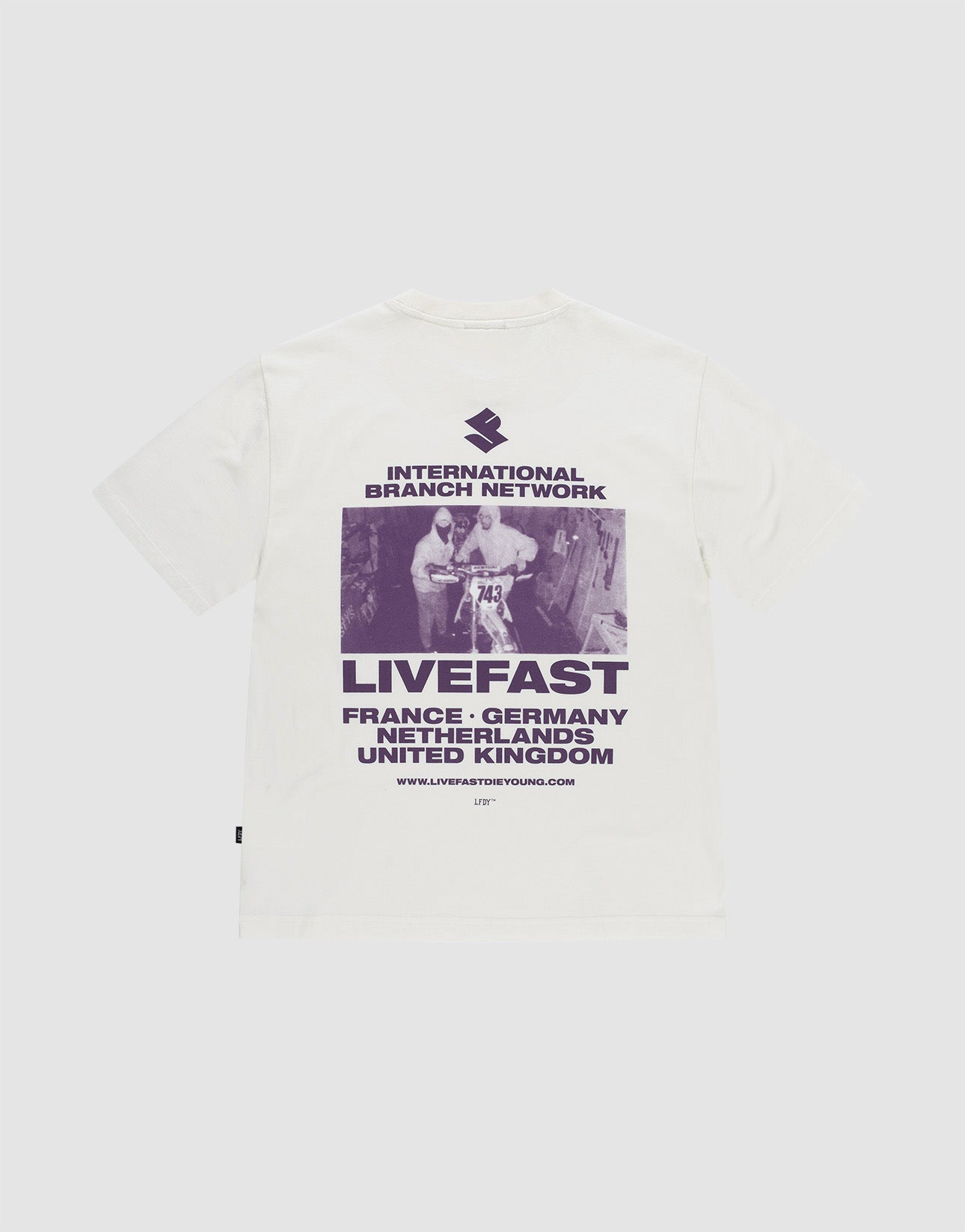 Das LFDY Grand Theft Tee von LIVE FAST DIE YOUNG ist ein weißes Oversize-Shirt aus 100% Baumwolle mit lila Backprint eines Skateboarders und Prints mit "INTERNATIONAL BRANCH NETWORK, LIVEFAST" sowie Ländernamen wie France und Germany.