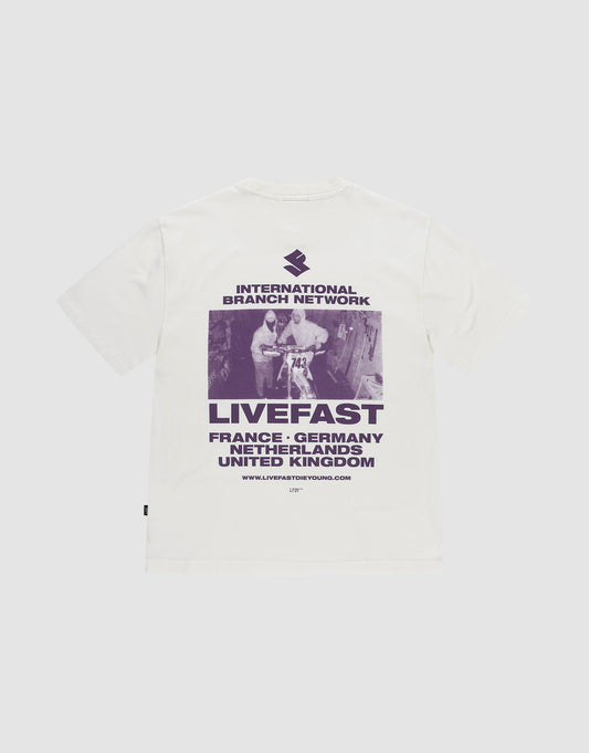 Das LFDY Grand Theft Tee von LIVE FAST DIE YOUNG ist ein weißes Oversize-Shirt aus 100% Baumwolle mit lila Backprint eines Skateboarders und Prints mit "INTERNATIONAL BRANCH NETWORK, LIVEFAST" sowie Ländernamen wie France und Germany. | plain