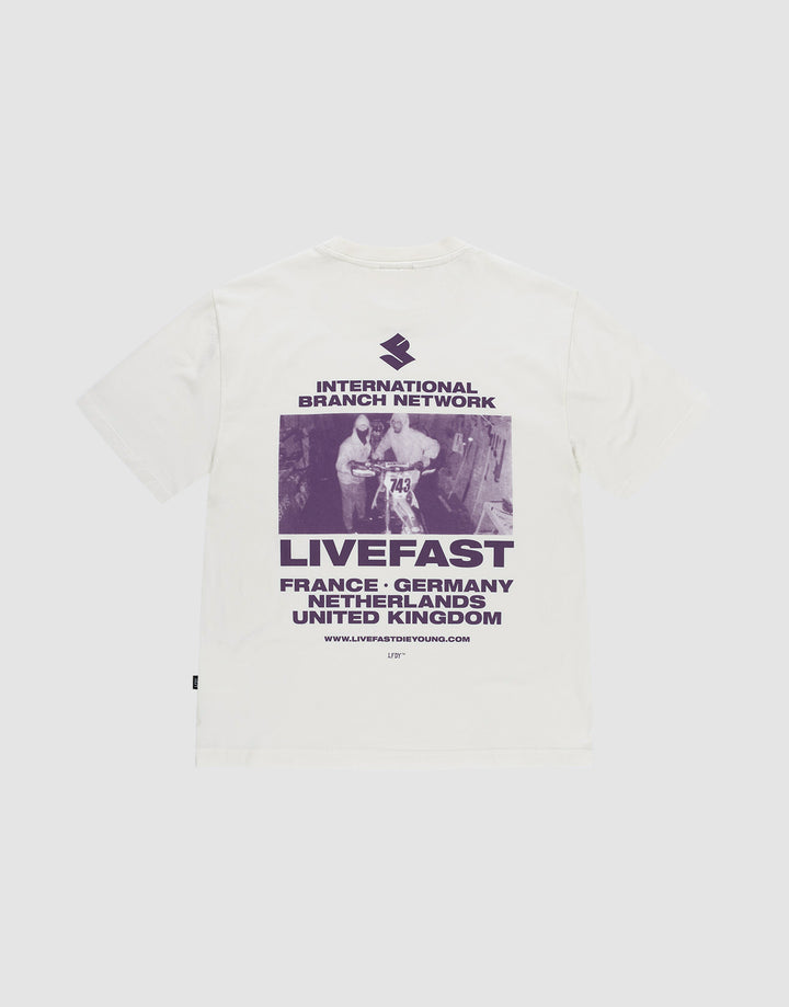 Das LFDY Grand Theft Tee von LIVE FAST DIE YOUNG ist ein weißes Oversize-Shirt aus 100% Baumwolle mit lila Backprint eines Skateboarders und Prints mit "INTERNATIONAL BRANCH NETWORK, LIVEFAST" sowie Ländernamen wie France und Germany. | plain