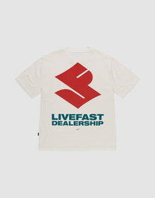 The LFDY Dealership Tee by LIVE FAST DIE YOUNG is an oversized white 100% cotton t-shirt, featuring a large red geometric backprint above bold blue "LIVEFAST DEALERSHIP" text and a small "LFTF" below, shown on a plain background. | plain