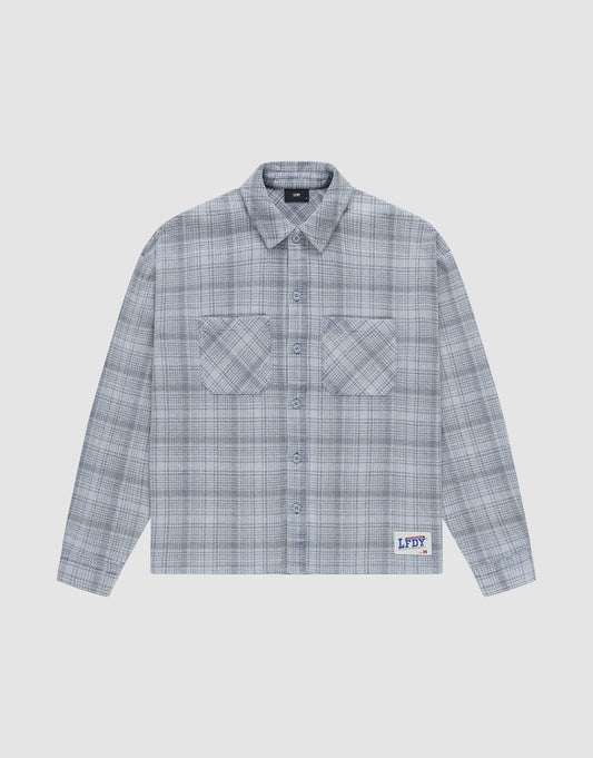 The Vintage Flannel by LIVE FAST DIE YOUNG is a gray plaid, long-sleeve, button-up shirt with two chest pockets and a small LFDY patch near the hem, featuring an oversize fit and vintage wash, shown laid flat on a white background. | plain