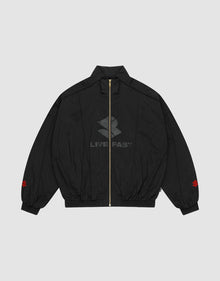 The LFDY Dealership Trackjacket by LIVE FAST DIE YOUNG is a black zip-up with Stehkragen, subtle LIVE FAST text and logo on the front, red sleeve logos near the cuffs, and a vergoldeter Reißverschluss. Background: light gray. | plain
