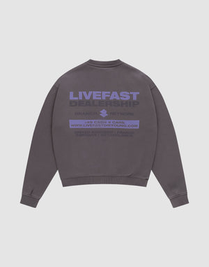 The LFDY Network Sweater von LIVE FAST DIE YOUNG ist ein graues Oversize-Crewneck aus Baumwolle mit lila "LIVEFAST DEALERSHIP" Backprint, weiteren Details, Website und Kleingedrucktem. Flach auf weißem Hintergrund präsentiert. | plain