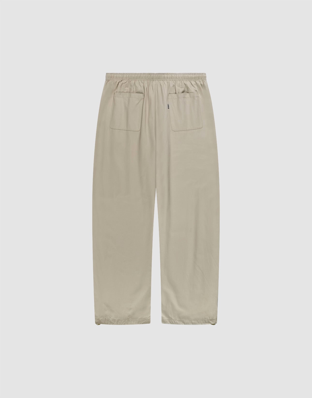 LIVE FAST DIE YOUNG Baggy Nylon Pants in beige, featuring a wide fit, elastic waistband, and two back patch pockets, shown flat on a plain light gray background.