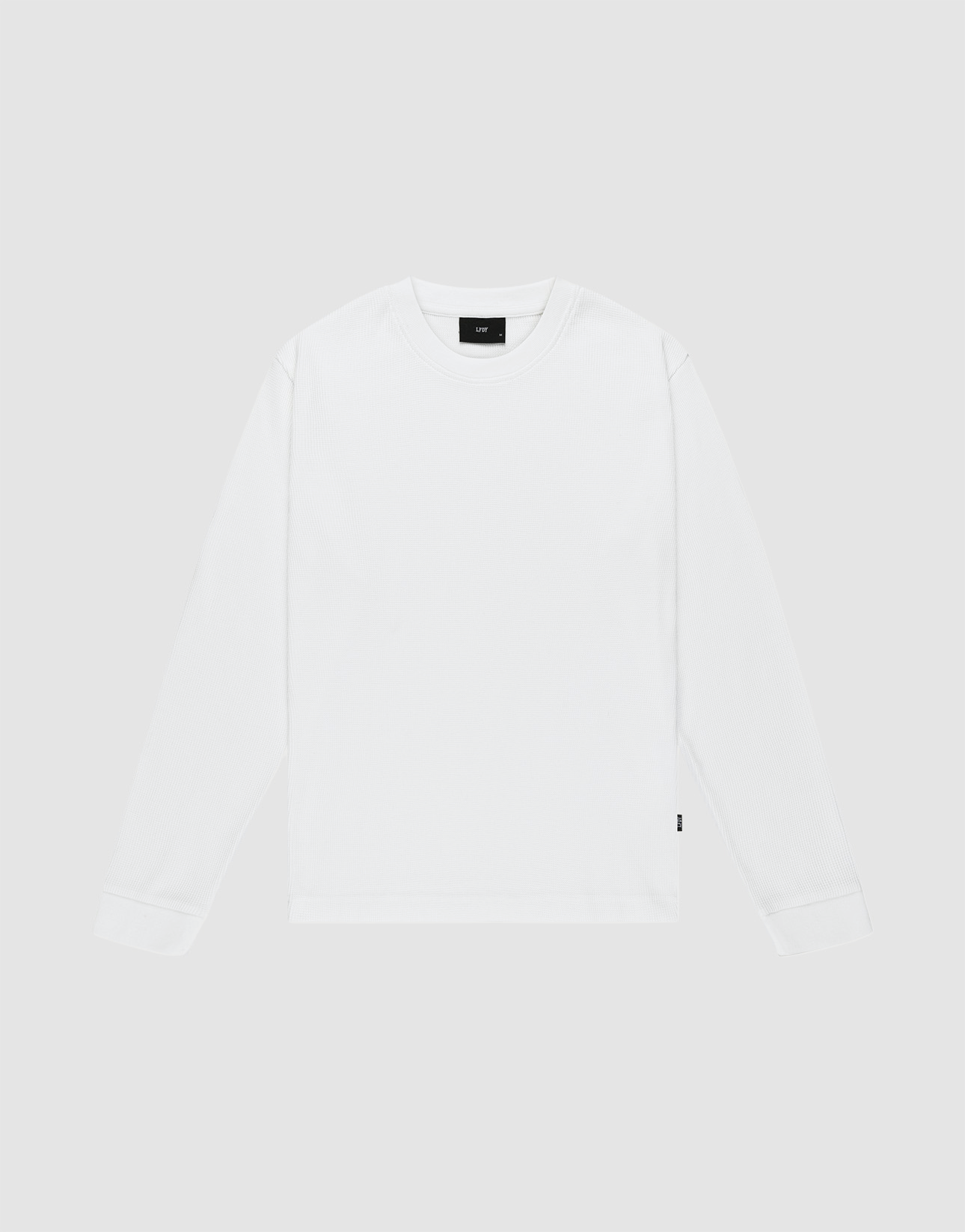The LIVE FAST DIE YOUNG Basic Waffle Longsleeve is an oversized, plain white crew neck shirt with long sleeves, laid flat on a light gray background. It features a small black flag-label on the lower side seam and no visible patterns or logos.