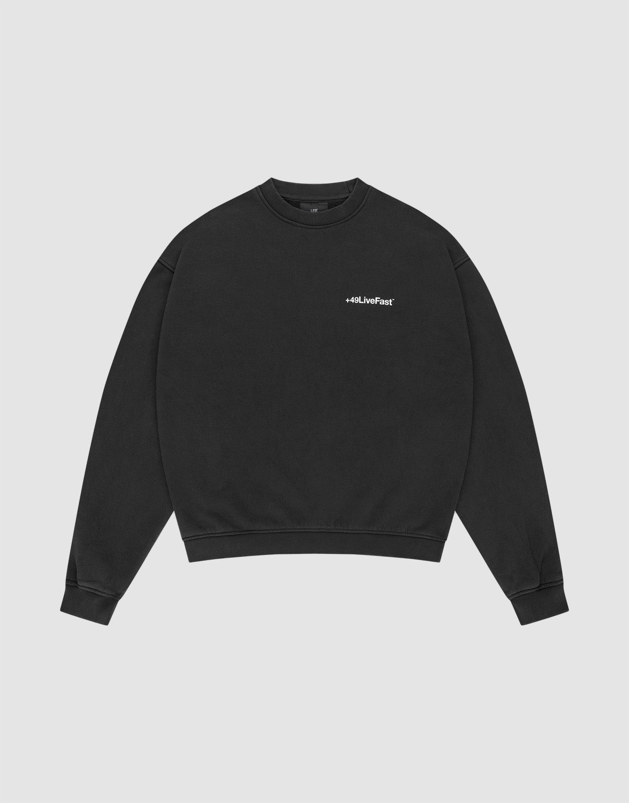 The LIVE FAST DIE YOUNG Basic +49 Chest Sweater is a black, oversized crewneck with ribbed cuffs and a small white #LLJLiveFast chest print, made from a cotton-polyester blend, shown flat on a light gray background.