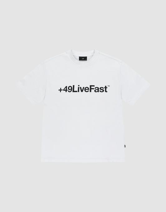 The Basic +49 Tee by LIVE FAST DIE YOUNG features a bold black “+49LiveFast™” front print on white, made from 100% Baumwolle, shown against a plain light grey background. | plain