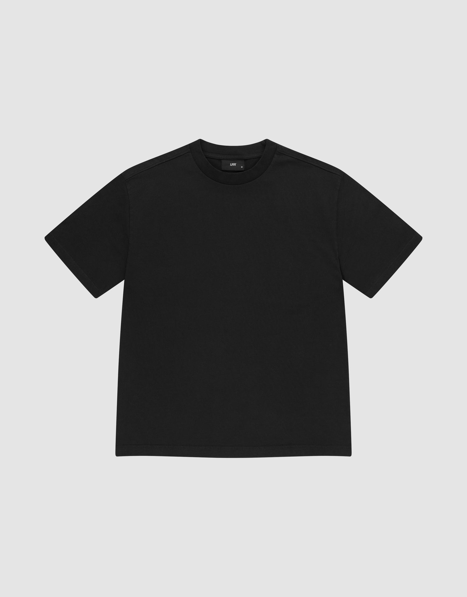 The LIVE FAST DIE YOUNG Basic Heavy Tee, a plain black short-sleeve shirt made from 100% Baumwolle, is shown laid flat on a light gray background with a classic crew neck and no visible logos or designs. | plain