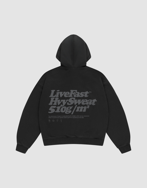 The Basic 510 Hooded Zip by LIVE FAST DIE YOUNG, in black Oversize Fit, is laid flat showing the back with bold gray "Live Fast. Hvy Sweat. 510g/m²" text plus smaller details, all on a plain light gray background. | plain