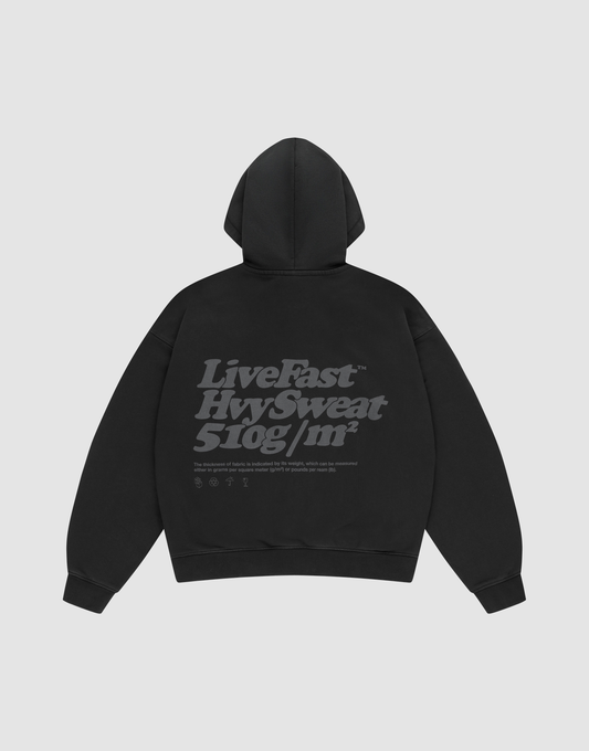 The Basic 510 Hooded Zip by LIVE FAST DIE YOUNG, in black Oversize Fit, is laid flat showing the back with bold gray "Live Fast. Hvy Sweat. 510g/m²" text plus smaller details, all on a plain light gray background. | plain