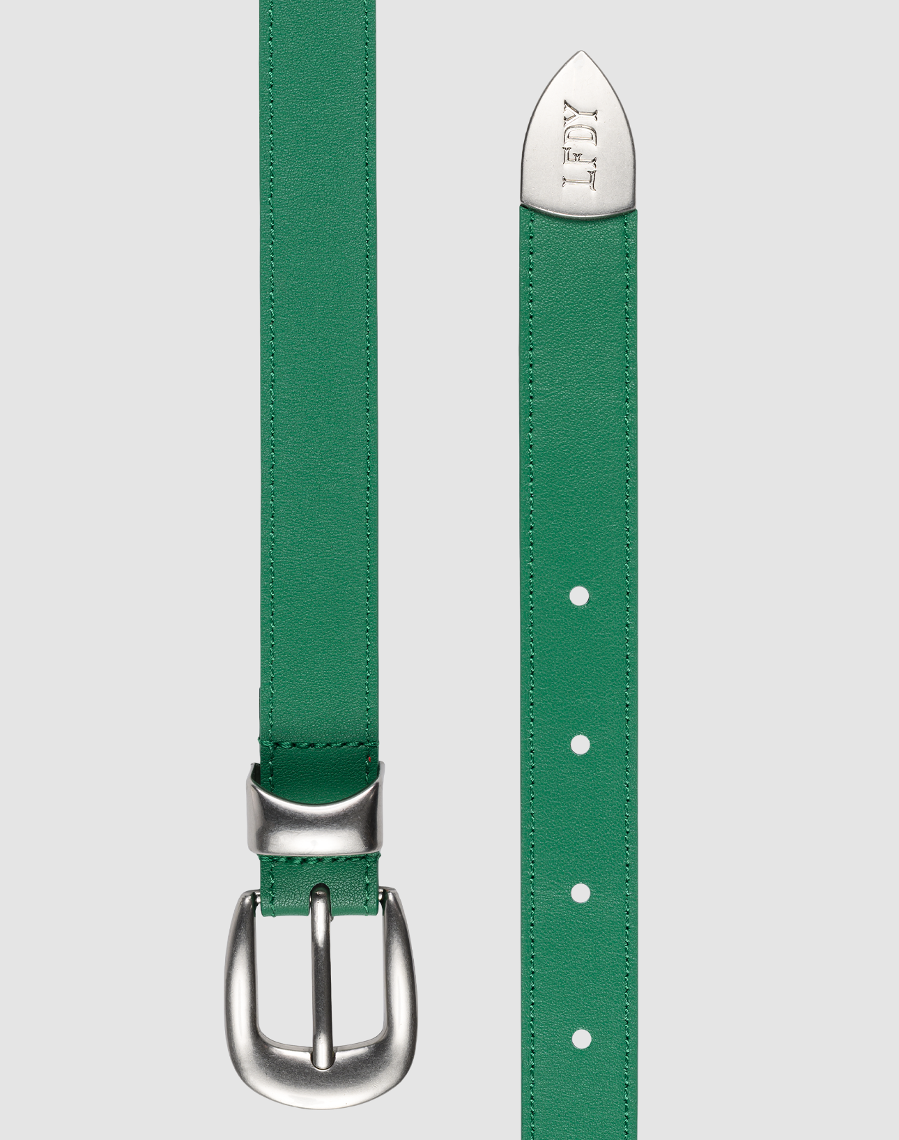 A green LFDY Slim Belt by LIVE FAST DIE YOUNG, featuring a silver buckle on the left and an engraved LOEWE logo on the pointed tip, is shown against a plain gray background. Gesamtlänge details are not visible.