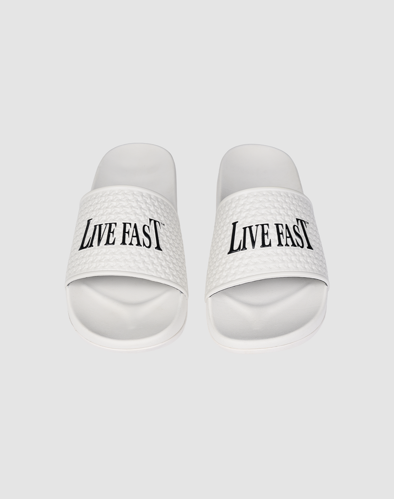 The LFDY Slides by LIVE FAST DIE YOUNG feature white PU textured straps with “LIVE FAST” in bold black letters, a comfortable EVA sole, and model number LF2606-20682.