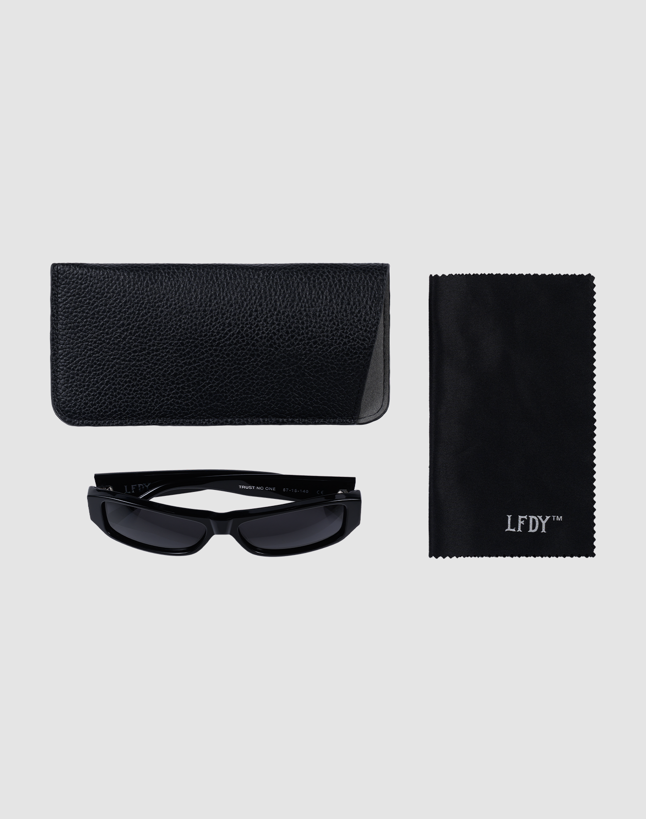 The LFDY Wrap by LIVE FAST DIE YOUNG: black rectangular sunglasses with UV-Schutz, a textured case, and a Reinigungstuch with white LFDY™ branding, all displayed on a light gray background.