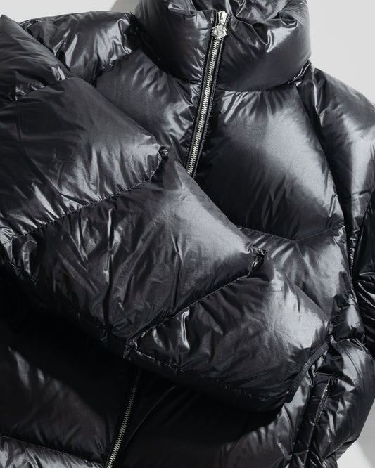 Close-up of the shiny black Live Fast Down Jacket by LIVE FAST DIE YOUNG, featuring a visible front zipper and quilted sections. The glossy, water-repellent fabric reflects light, accentuating its puffy texture and modern style.