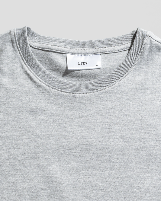 A close-up of the LFDY Slim Tee by LIVE FAST DIE YOUNG in plain light gray, featuring a collar with a white neck tag showing LFDY, size M, Flag-Label details, and crafted from soft Baumwolle.