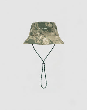 The LIVE FAST DIE YOUNG Camo Nylon Bucket Hat in green camouflage features strapazierfähigem Nylon Stoff, a white silicone LIVE FAST print on the front, and a matching green Kinnband, shown on a plain white background.