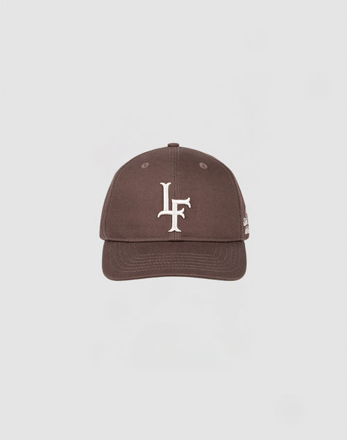The LF Snapback by LIVE FAST DIE YOUNG is a brown baseball cap made from 100% Baumwolle, featuring a white LF logo embroidered on the front and a snap closure. It is centered against a plain light gray background.