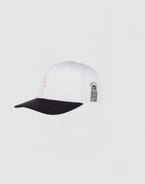 The LF Snapback by LIVE FAST DIE YOUNG is a white baseball cap with a black brim and underside, featuring a stylized LF logo on the front and a small Statue of Liberty graphic with Liner East Wind text on the side. Snap closure ensures perfect fit.