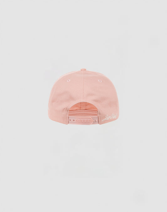 The LF Snapback by LIVE FAST DIE YOUNG is a light pink cotton baseball cap, shown from the back with a snap closure and white embroidered logo in script near the edge.