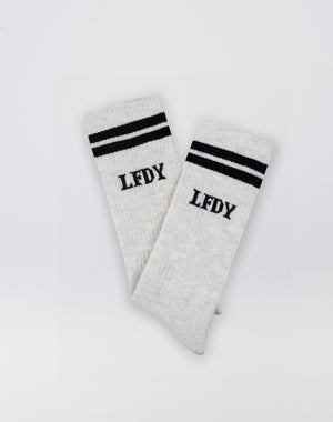 The LIVE FAST DIE YOUNG Basic Socks (2 Pack) are white, crafted from a soft Baumwolle blend, with two black stripes near the top and LFDY printed below, shown against a plain white background.