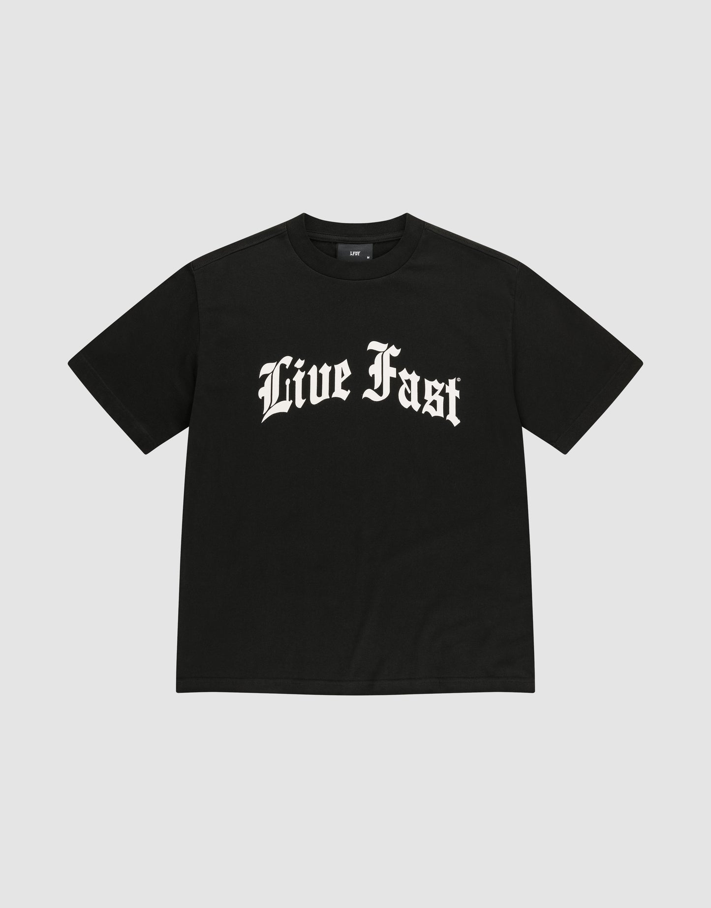 The Live Fast Fractured Tee by LIVE FAST DIE YOUNG is a black, oversized 100% cotton t-shirt with short sleeves and bold “Live Fast” white Gothic lettering on the chest, shown against a plain light gray background.