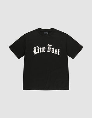 The Live Fast Fractured Tee by LIVE FAST DIE YOUNG is a black, oversized 100% cotton t-shirt with short sleeves and bold “Live Fast” white Gothic lettering on the chest, shown against a plain light gray background. | plain