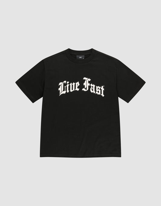 The Live Fast Fractured Tee by LIVE FAST DIE YOUNG is a black, oversized 100% cotton t-shirt with short sleeves and bold “Live Fast” white Gothic lettering on the chest, shown against a plain light gray background. | plain