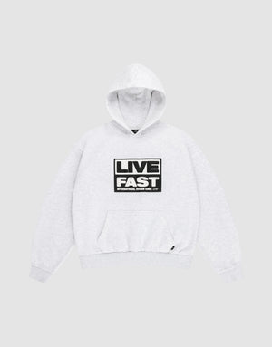 The LIVE FAST DIE YOUNG Live Fast Box Hooded sweatshirt, shown laid flat on a gray background, features an oversized fit, front pocket, and bold black and white “LIVE FAST” puffer print with smaller text beneath on the chest. | plain