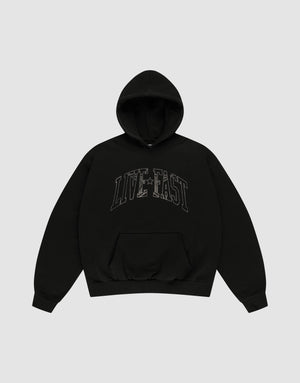 The LIVE FAST DIE YOUNG Live Fast Rhinestone Hooded is a black oversized hoodie with a double-layered hood, front pocket, and bold "LIVE FAST" outlined letters across the chest. The background is plain light gray. | plain
