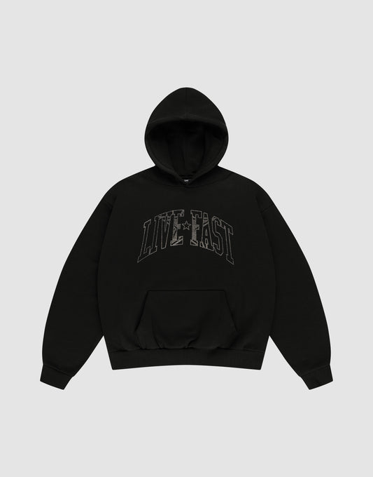 The LIVE FAST DIE YOUNG Live Fast Rhinestone Hooded is a black oversized hoodie with a double-layered hood, front pocket, and bold "LIVE FAST" outlined letters across the chest. The background is plain light gray. | plain