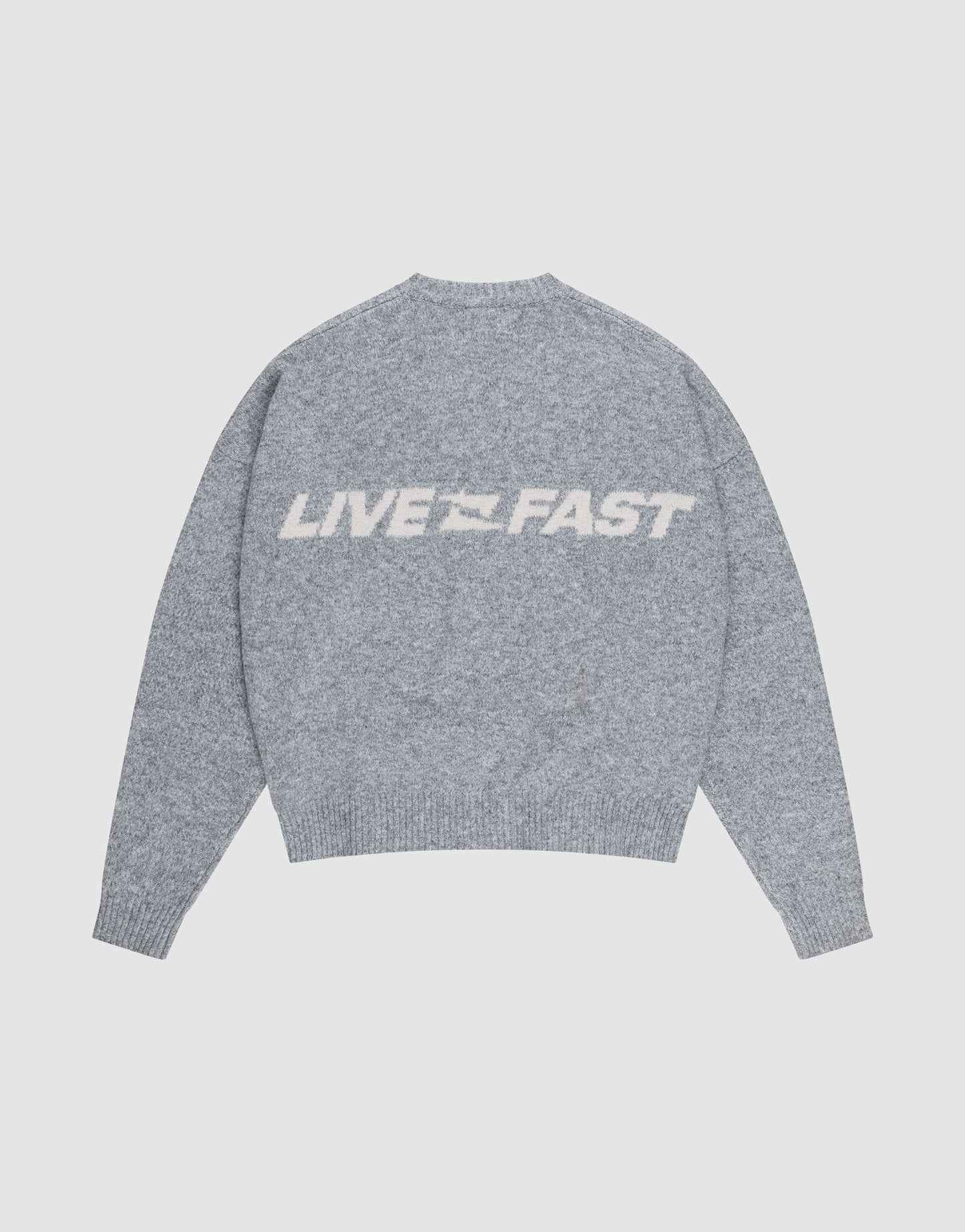 The Live Fast Boucle Sweater by LIVE FAST DIE YOUNG is a gray oversized knit with a crew neck, ribbed cuffs, and "LIVE FAST" in large white letters across the back. Made of 100% polyester.