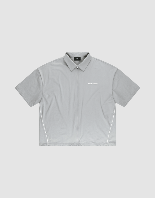 The LFDY Ripstop Shirt by LIVE FAST DIE YOUNG is a light gray, oversize-fit zip-up shirt with white side piping and a small "LIVE FAST" silicone print on the left chest, shown laid flat on a plain background. | plain