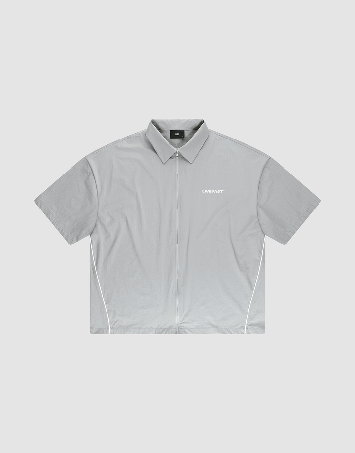 The LFDY Ripstop Shirt by LIVE FAST DIE YOUNG is a light gray, oversize-fit zip-up shirt with white side piping and a small "LIVE FAST" silicone print on the left chest, shown laid flat on a plain background. | plain