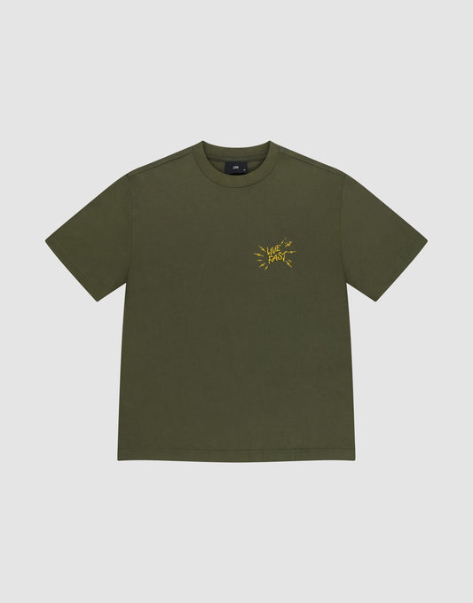 Das LFDY Against Us Tee von LIVE FAST DIE YOUNG ist ein olivgrünes Oversize-T-Shirt aus 100% Baumwolle mit gelbem Frontprint und "LIVE FAST" Schriftzug auf der linken Brust, präsentiert vor hellem Hintergrund.