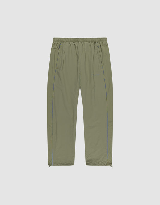 The Live Fast Trackpants by LIVE FAST DIE YOUNG are light olive green, wide-fit, lightweight pants with an elastic waistband, side pockets, subtle seam details, ankle zippers, and a reflective logo print. Shown on a plain white background. | plain