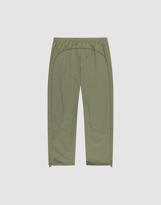 The Live Fast Trackpants by LIVE FAST DIE YOUNG feature a light olive green color, elastic waistband, straight-leg wide fit, blue side piping, reflective logo print, and small side zippers at the leg openings on a light background.
