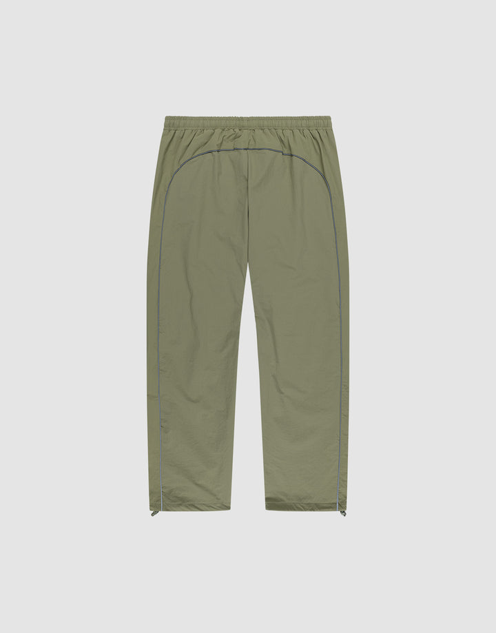 The Live Fast Trackpants by LIVE FAST DIE YOUNG feature a light olive green color, elastic waistband, straight-leg wide fit, blue side piping, reflective logo print, and small side zippers at the leg openings on a light background.
