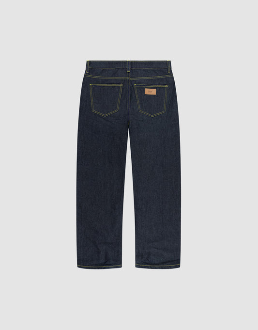 The LIVE FAST DIE YOUNG Work Denim jeans feature a straight-leg cut in dark blue raw denim, two rear pockets with yellow stitching, and a brown leather waistband patch, shown from the back.