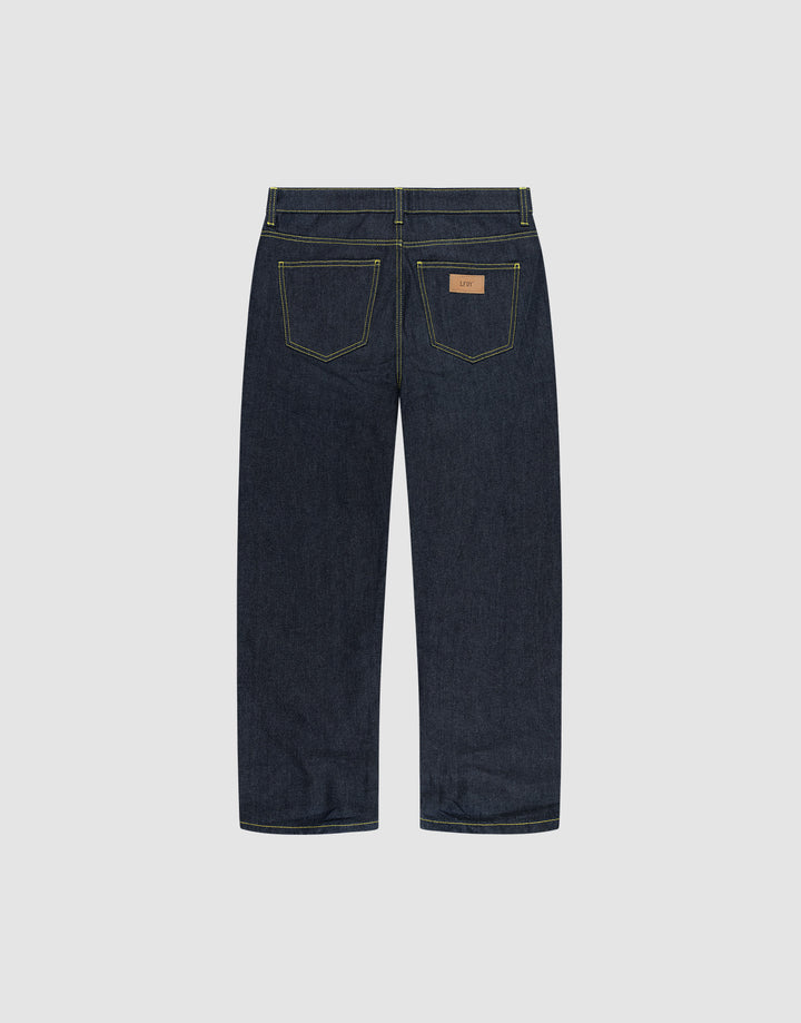 The LIVE FAST DIE YOUNG Work Denim jeans feature a straight-leg cut in dark blue raw denim, two rear pockets with yellow stitching, and a brown leather waistband patch, shown from the back.